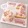 Olivia butterfly-themed Celebration Board with a pastel pink and lilac mini cake, layered number 1 cookie cake, flowers, butterflies and personalised first birthday message.