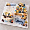 Construction-themed Soeterie Celebration Board with a round mini cake, layered number 4 cookie cake, yellow diggers, trucks, traffic cones and personalised birthday details on a square board.