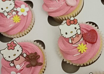 Close-up of pink Hello Kitty cupcakes decorated with character toppers, a bow, heart, teddy bear and flowers.