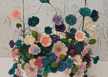 White cake surrounded by pink, teal, purple and ivory flowers, with tall floral stems and silver accents.