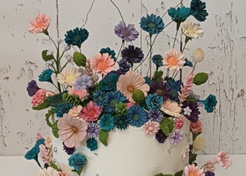White floral wedding cake with tall flower stems, pink and purple blossoms, teal flowers and green leaves.