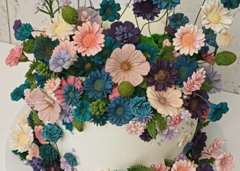 Close-up of a white wedding cake surrounded by pink, teal, purple and ivory flowers with silver accents.