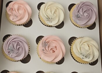 Box of cupcakes with alternating lilac, blush pink and ivory frosting swirls, decorated with silver pearls and glitter.